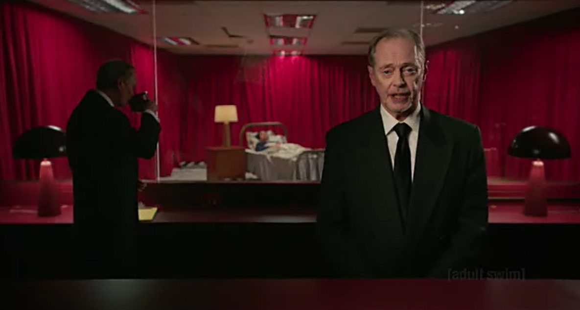 Steve Buscemi in a black suit in front of red curtains, with a man asleep in a hospital bed behind him