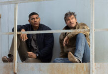 HBO’s “Lanterns” Review: The Green Lantern Series Gets Much Better "Lanterns" Aaron Pierre and Kyle Chandler sit on a metal railing, looking pensively into the distance against a weathered backdrop.