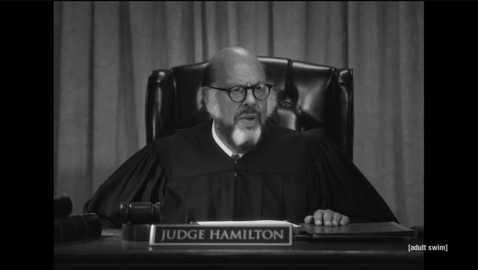 Fred Melamed as Judge Hamilton behind the bench, in black and white.