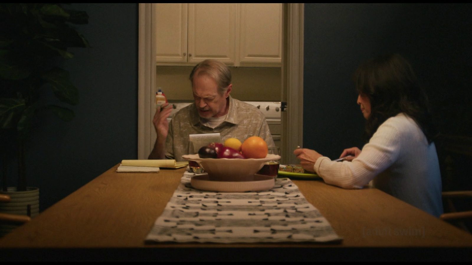 Steve Buscemi at the dinner table surrounded by notepads as Lauren Tom eats beside him
