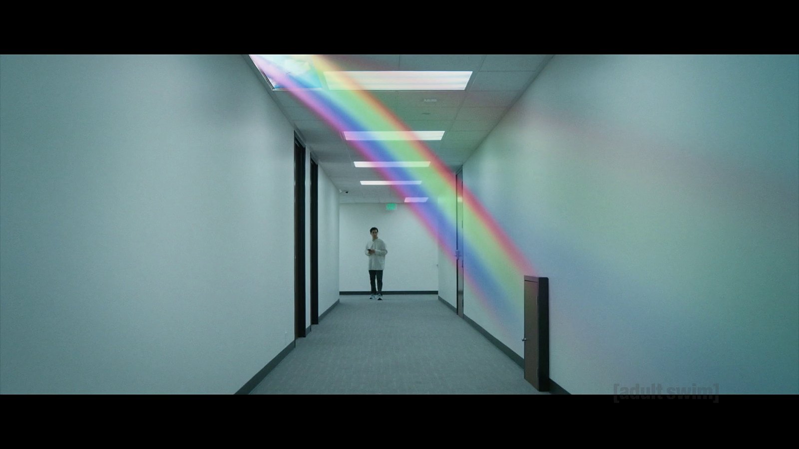 Jordan Mendoza ad the end of a hallway, staring at a tiny door lit by a rainbow from a skylight