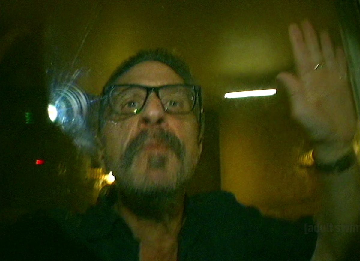 Marc Maron at a podcast microphone inside a glass cell, across from a patient in a gown