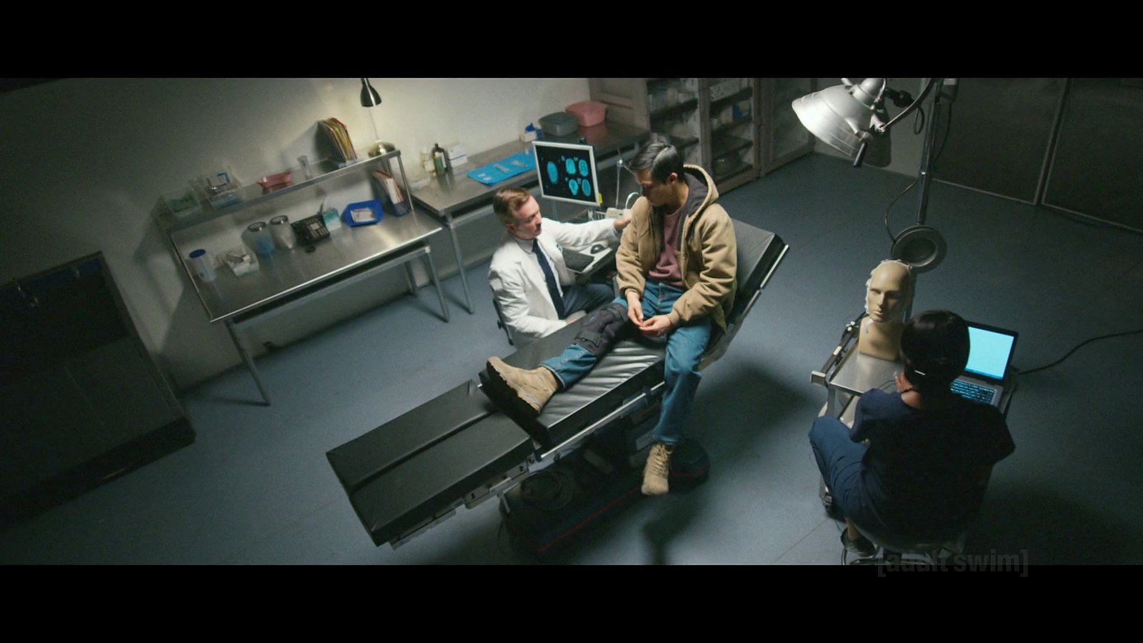 Jordan Mendoza on a medical table with Thomas Lennon as the doctor beside him