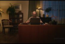 Steve Buscemi at a desk in a lamplit home office, searching on his laptop